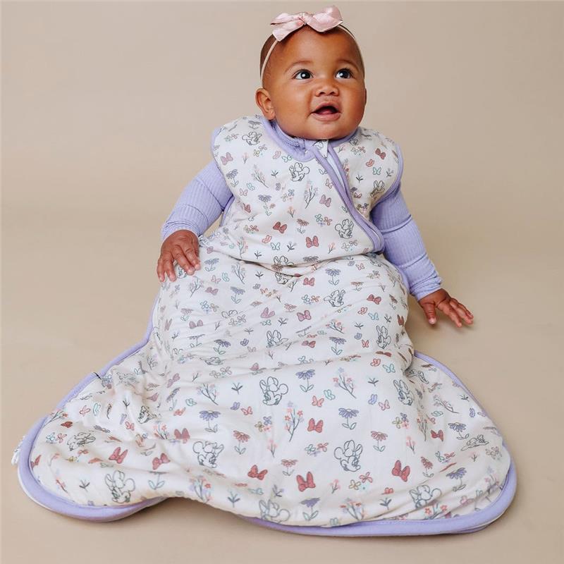 Baby wearing a Copper Pearl Minnie Mouse Bowquet sleep bag, featuring floral and butterfly patterns, smiling while seated.