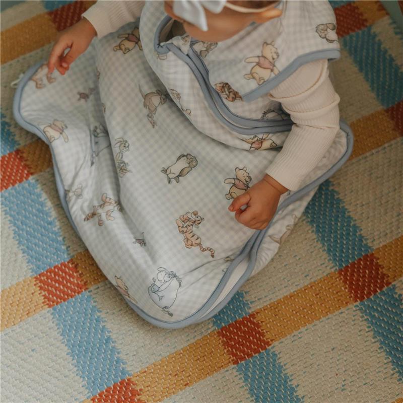 Premium 3-layer knit sleep bag featuring Winnie the Pooh and friends, worn by a baby on a colorful woven rug.