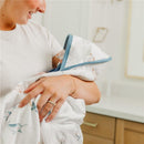 A woman holds a baby wrapped in a Copper Pearl Premium Baby Knit Hooded Towel with animal prints and a blue trim.