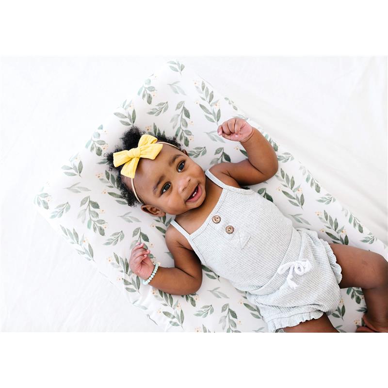 Soft fern-patterned changing pad cover featuring a smiling baby wearing a gray outfit and a yellow bow in her hair.