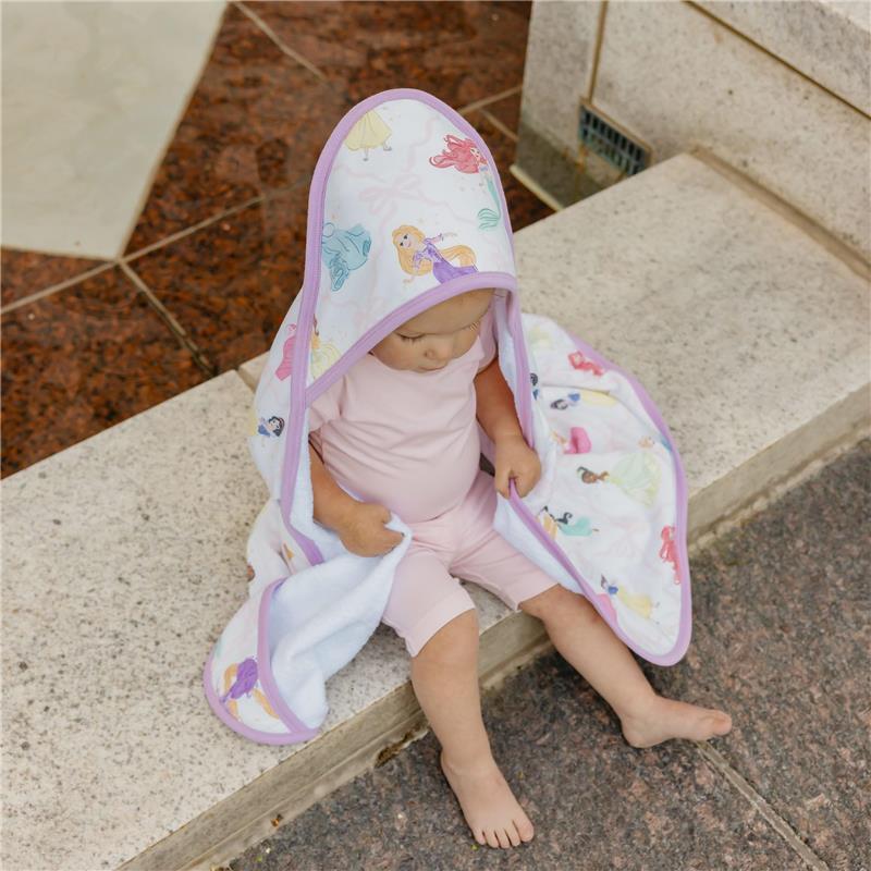Hooded bath towel featuring Disney Princess designs, used by a child sitting on a stone surface.