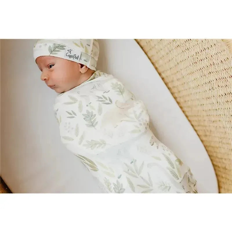 Newborn swaddled in a soft, patterned receiving blanket and matching hat, resting on a light surface.