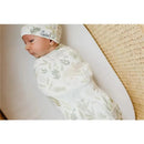 Newborn swaddled in a soft, patterned receiving blanket and matching hat, resting on a light surface.