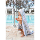 Toddler in a hooded copper pearl bath towel with floral pattern, standing by a pool, gripping a railing.