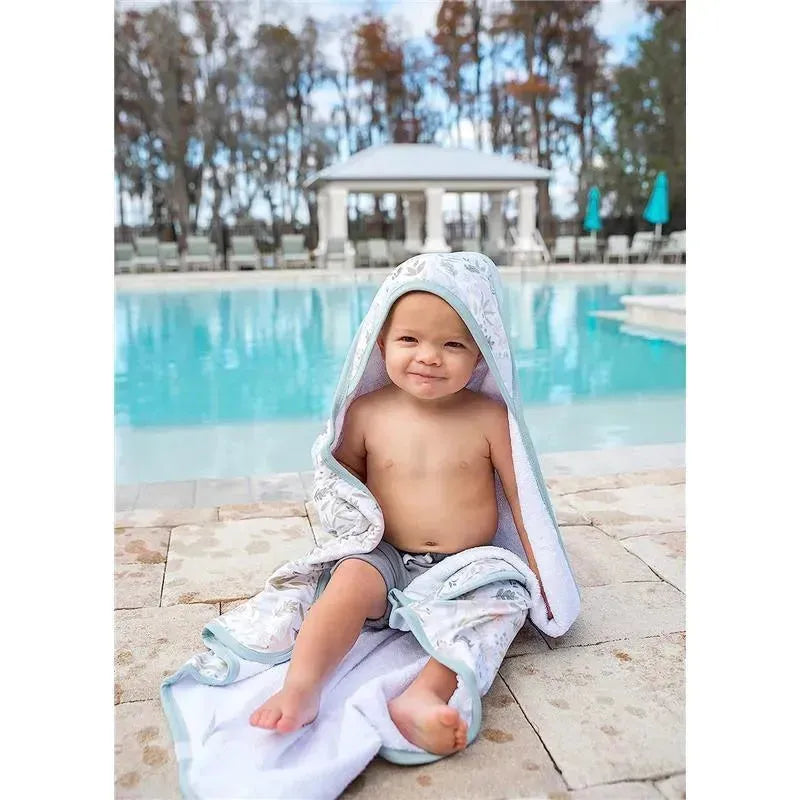 Toddler sitting by a pool, wearing a hooded Copper Pearl towel with a floral design.