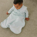 Light blue 0.5 Tog sleep bag designed for infants, worn by a baby sitting on a carpeted floor.