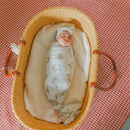 A wrapped baby sleeping peacefully in a woven bassinette, covered with a Copper Pearl Winnie the Pooh knit blanket.