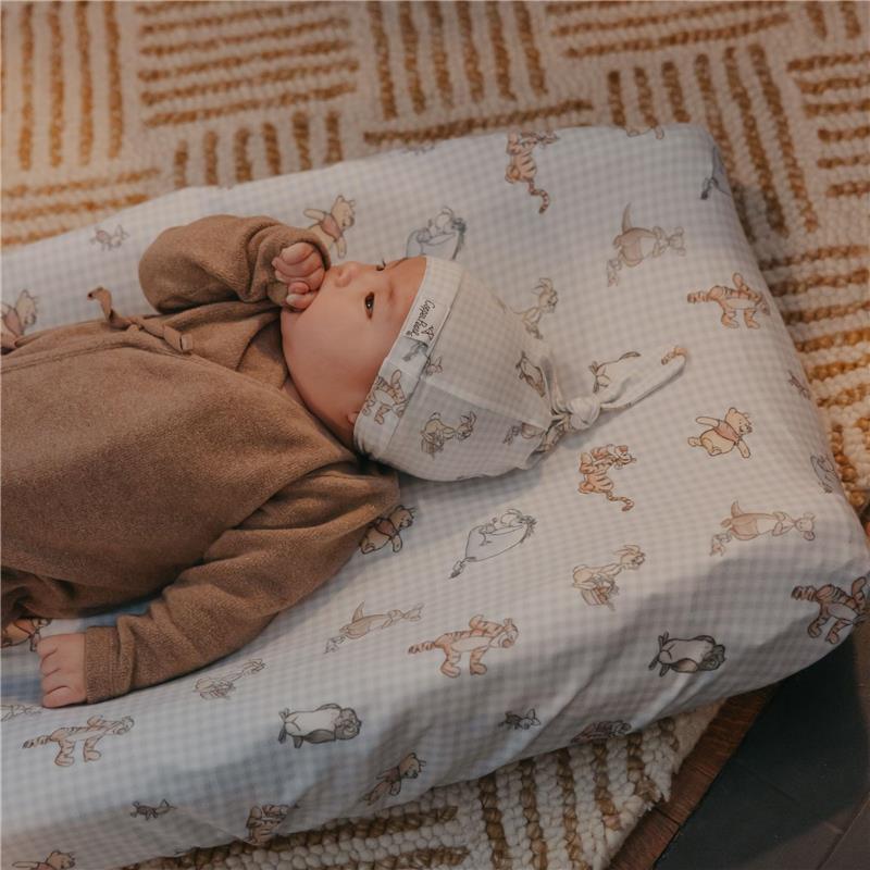 Premium diaper changing pad cover featuring Winnie the Pooh and friends, with a baby lying on it, wearing a matching hat.