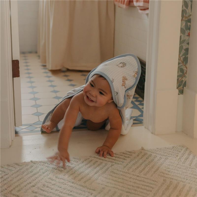 A smiling baby in a Copper Pearl Winnie The Pooh hooded towel crawls on the floor, reaching out playfully.