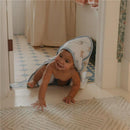 A smiling baby in a Copper Pearl Winnie The Pooh hooded towel crawls on the floor, reaching out playfully.