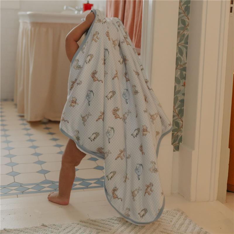 A child wearing a hooded towel featuring Winnie The Pooh characters walks in a bathroom, showcasing its cute design.
