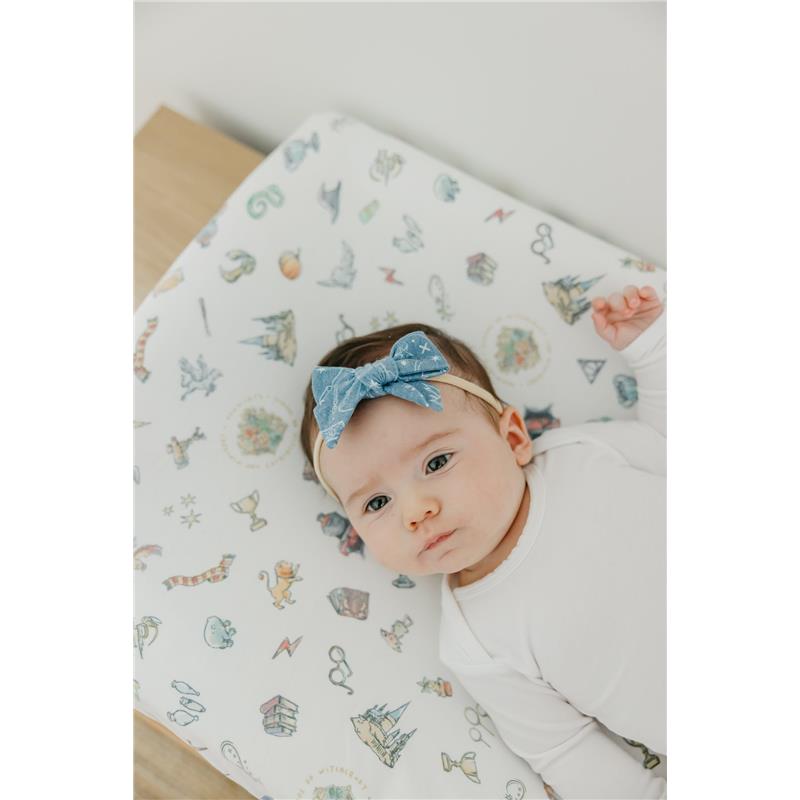 Premium diaper changing pad cover featuring whimsical Wizarding World™ designs, with a baby wearing a blue bow headband.