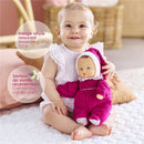 A smiling baby sits on a mat, holding a Corolle Babipouce doll in a pink outfit with a vanilla scent.