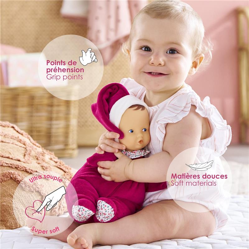 Infant in a ruffled white outfit hugging a Corolle Babipouce doll in pink with soft materials, highlighting grip points.