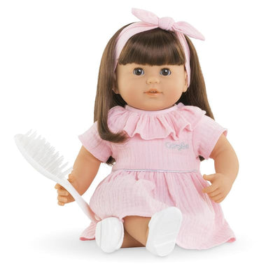 Julie is a 14-inch Corolle baby girl doll with brown hair, dressed in a pink ruffled dress, holding a white hairbrush.
