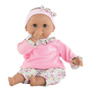Bébé Calin Maria baby doll by Corolle, dressed in a pink top and floral pants, sitting and sucking her thumb.