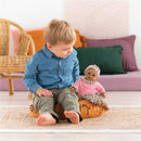 Child sitting on a cushion, holding the Corolle Bébé Calin Maria baby doll dressed in a pink outfit with floral details.