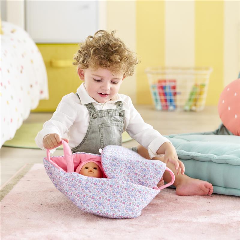 Child playing with a Corolle Dolls Floral Moses Basket, cradling a 30 cm doll wrapped in a floral blanket.