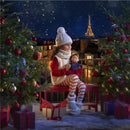 Girl in winter attire sitting on a red bench holds a Corolle Ma Perle doll, with decorated Christmas trees and the Eiffel Tower in the background.