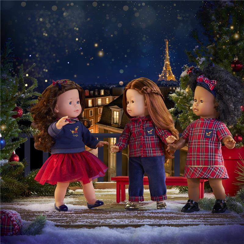 Three Corolle dolls in festive outfits gather in a winter scene with a decorated tree and the Eiffel Tower in the background.