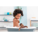 A young child plays with the Corolle Mon Premier Poupon Bath Baby Alyzee in a bathtub filled with bubbles.