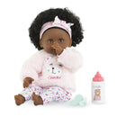 12-inch Corolle Baby Calin Caroline doll with curly black hair, dressed in a pink bear sweatshirt and patterned pants, holding thumb to mouth. Includes a bottle and accessories.