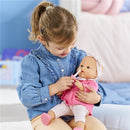 A girl in a denim shirt uses a toothbrush to care for a doll dressed in a pink top with a bow, showcasing the Corolle Dolls Tulip Changing Accessory Set.