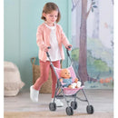 Young girl in a pink cardigan pushes a pink striped Corolle Dolls umbrella stroller containing a baby doll.