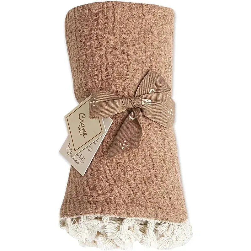 Copper red muslin swaddle blanket by Crane, featuring a textured design and a decorative tassel edge, tied with a ribbon.