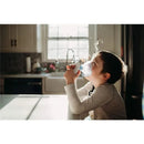 Child using a Crane cordless warm and cool mist inhaler, exhaling mist in a sunlit kitchen.