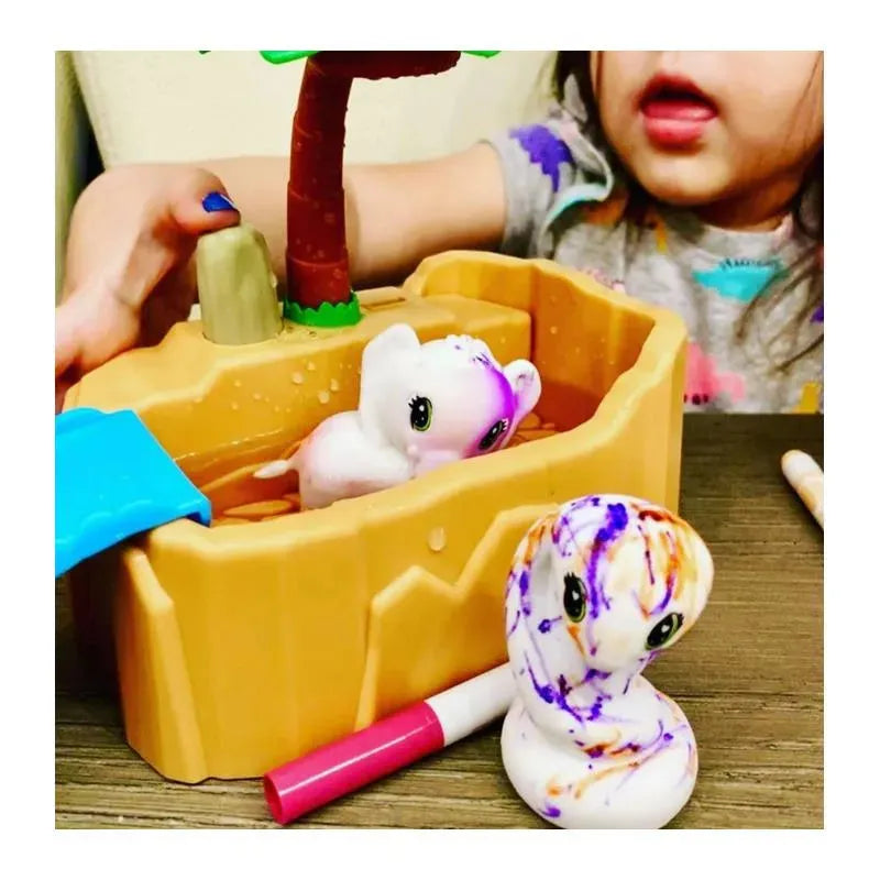 Crayola Scribble Scrubbie Safari with a child’s hand holding a toy in a playset featuring colorful, washable animal figures in a watering hole.
