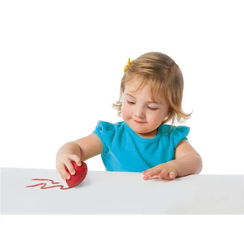 Child using a red Crayola washable egg crayon to draw a wavy line on a white surface.