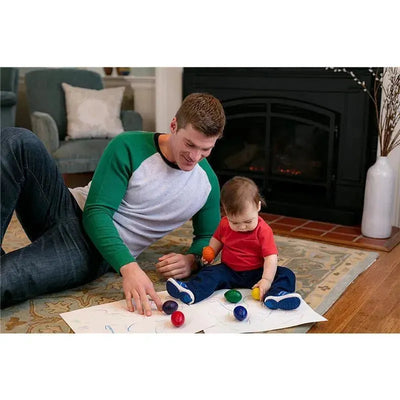 Father and toddler sitting on the floor with colorful crayons and drawings on paper, engaging in creative playtime.