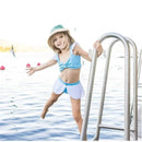 A young girl in a blue and white two-piece swimsuit, smiling while climbing a pool ladder near water.