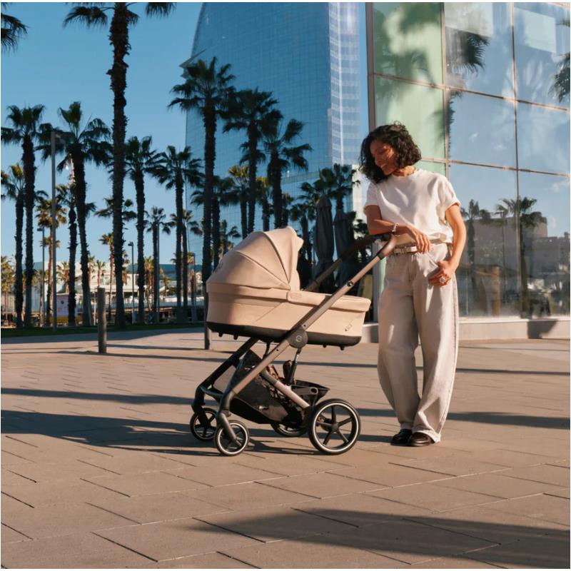 Cybex Balios S Lux Stroller in Stone Grey, pushed by a woman in casual attire, amidst palm trees and modern architecture.