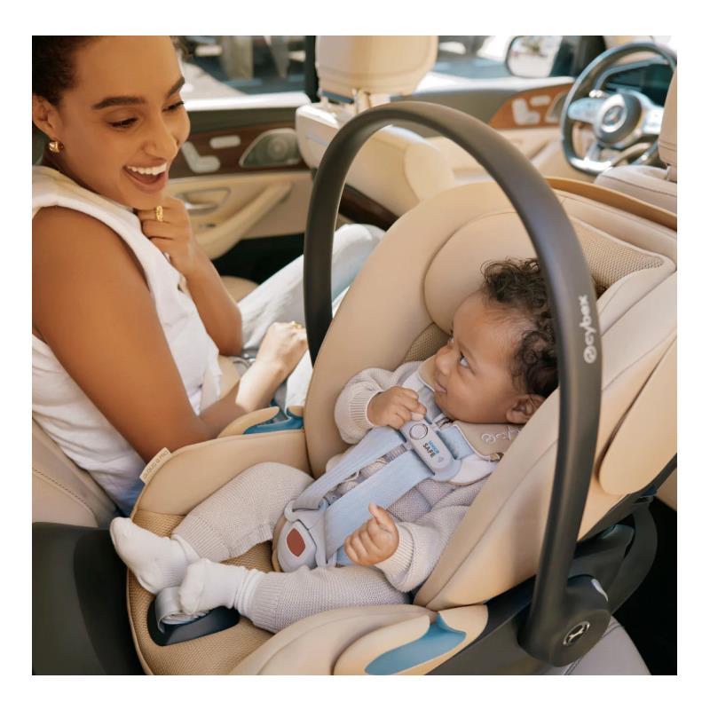 Cybex Cloud G Pro Comfort Extend Infant Car Seat in Almond Beige with a baby securely fastened and a smiling parent in a car.