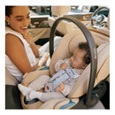 Cybex Cloud G Pro Comfort Extend Infant Car Seat in Almond Beige with a baby securely fastened and a smiling parent in a car.