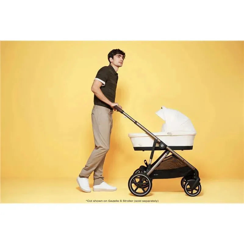 Cybex Gazelle S Cot in Seashell Beige being pushed by a man against a yellow background.