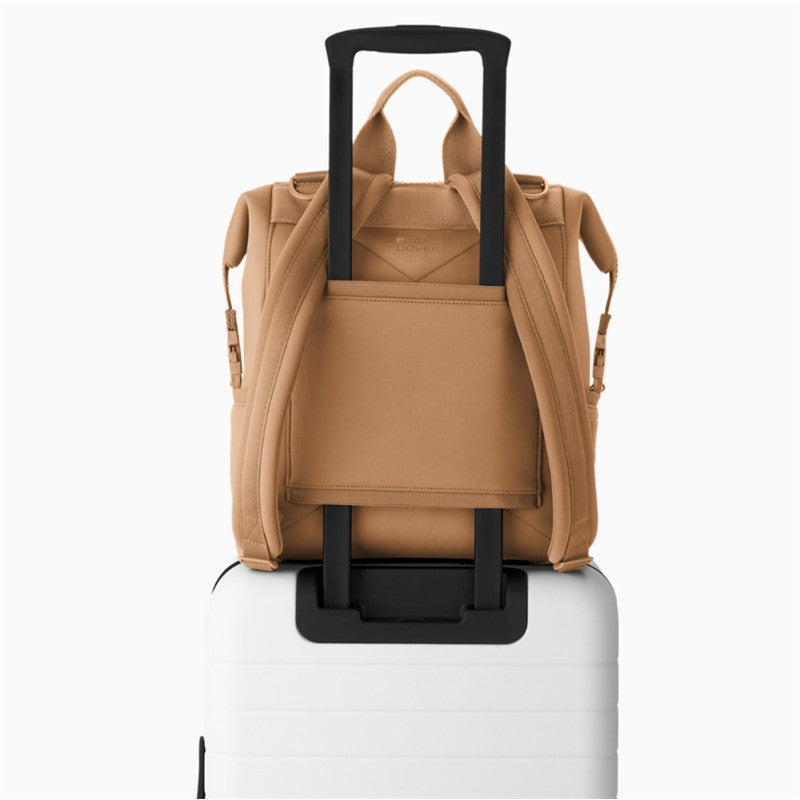 Camel-colored Dagne Dover Indi Diaper Backpack mounted on a white suitcase, showcasing its sleek design and practicality.