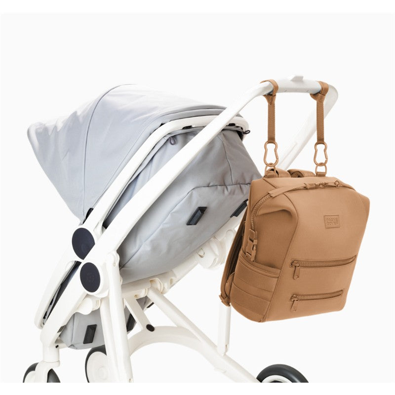 Dagne Dover Indi Diaper Backpack in camel hangs on a white stroller, showcasing its medium size and multiple zippered pockets.