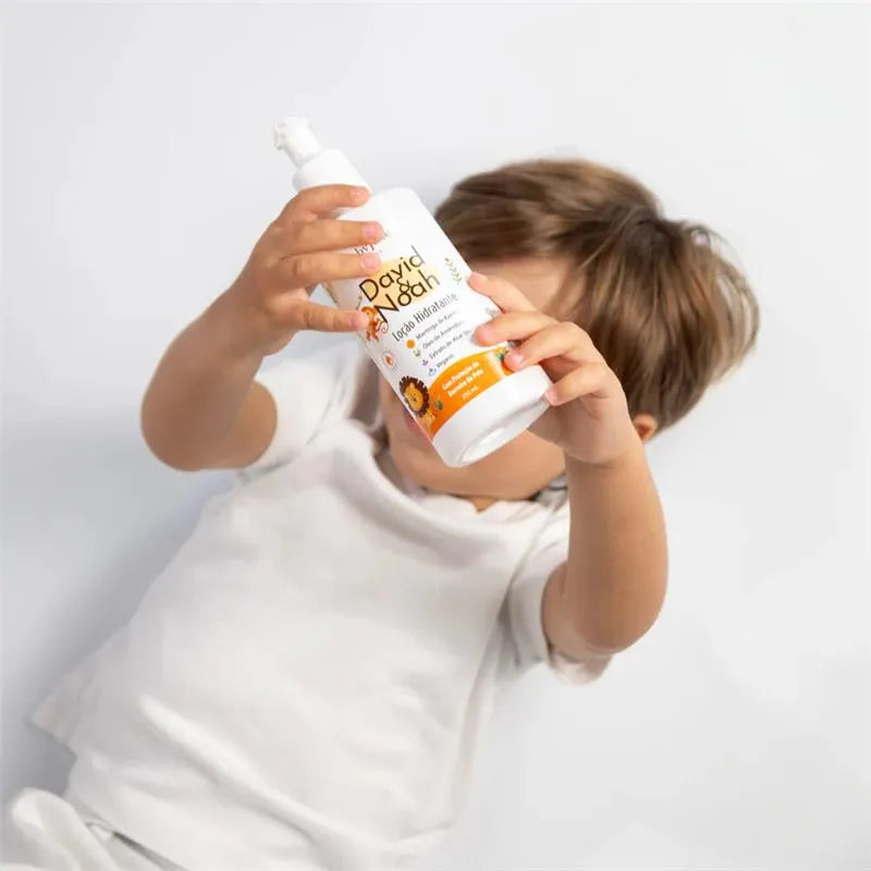 Child holding David & Noah By Baby Jolie Body Lotion, featuring bright packaging and a playful design, on a light background.