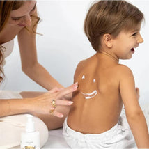 A woman applies lotion to a child’s back, which has a smile drawn on it, promoting the David & Noah lotion bundle.