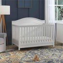 DaVinci Charlie 4-In-1 Convertible Baby Crib in white, featuring a slatted design and curved headboard, set in a cozy nursery.