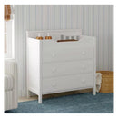 White three-drawer dresser with changing top, featuring bottles and a basket, in a light-colored nursery setting.