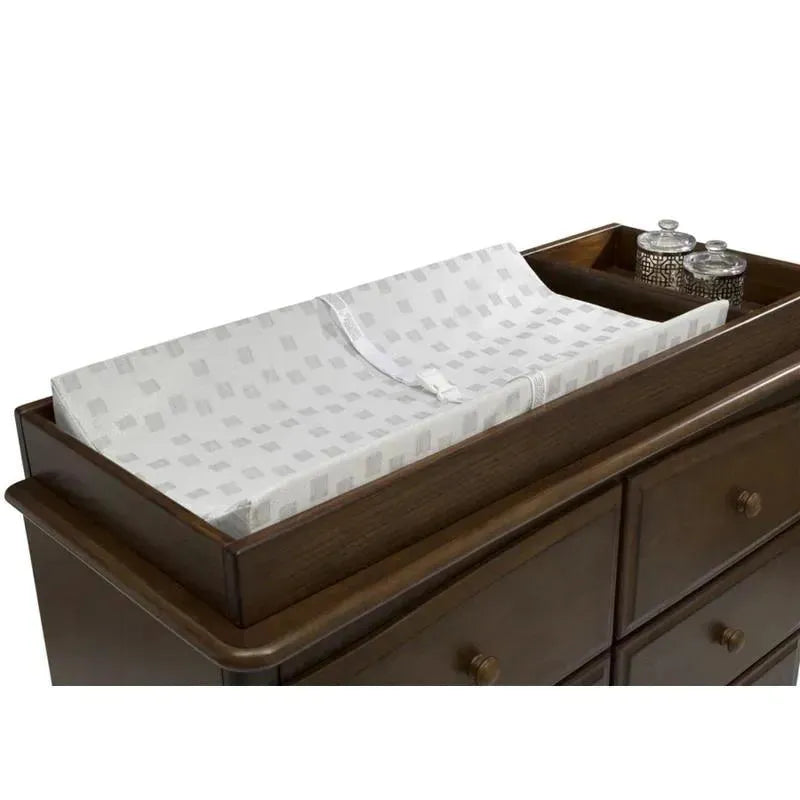 Waterproof contoured changing pad by Delta Children on a wooden dresser, featuring a white cover with gray patterns.