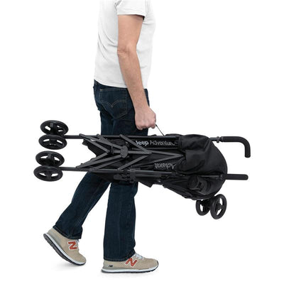 A person carrying a folded Delta Jeep Adventureglyde stroller in black and grey.