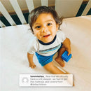 Toddler sitting on a crib mattress pad, smiling and holding a blue block, showcasing the Delta Sertapedic product.