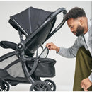 A man adjusts the canopy of a DFY - R1 Cool Box Black stroller while inspecting its mesh storage area.