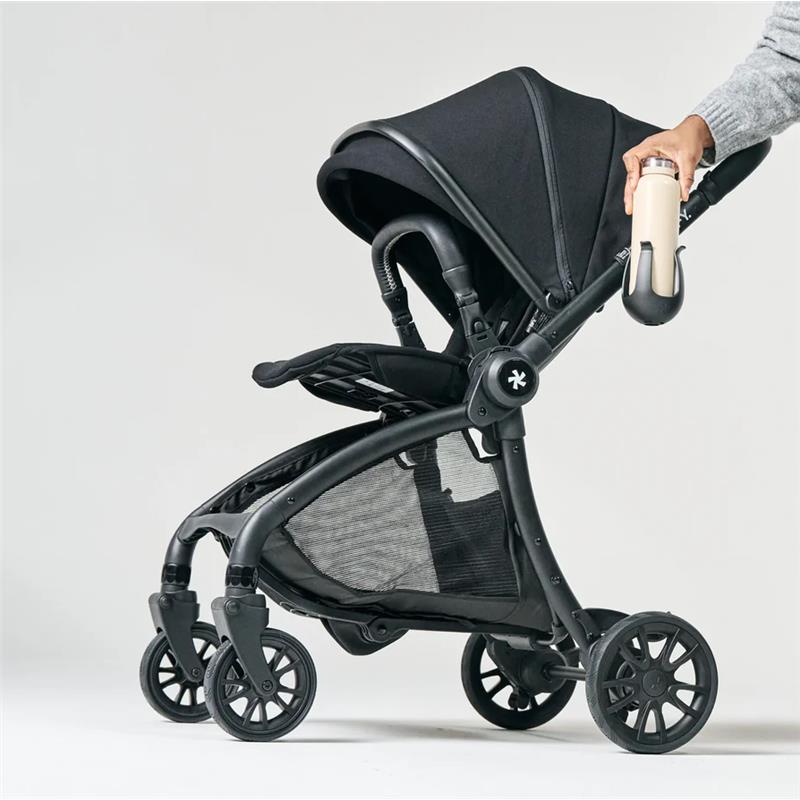 Black R1 Cup Holder attached to a stroller, with a hand holding a beverage container, showcasing its practical design.