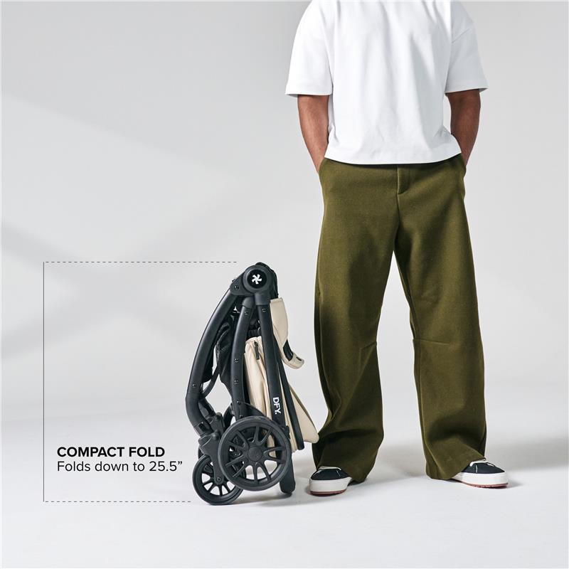 Cream DFY - R1 single stroller, compactly folded, displayed beside a person wearing olive pants and a white shirt.